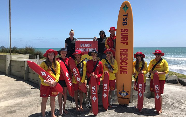 A group of lifeguards standing with their boards in front of a beach
