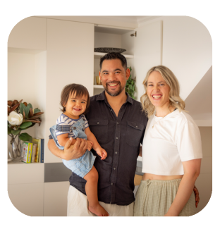 young couple holding their child smiling standing in their first home