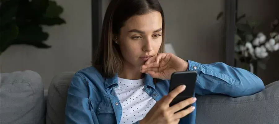 Serious woman sitting on sofa looking at smartphone and is upset