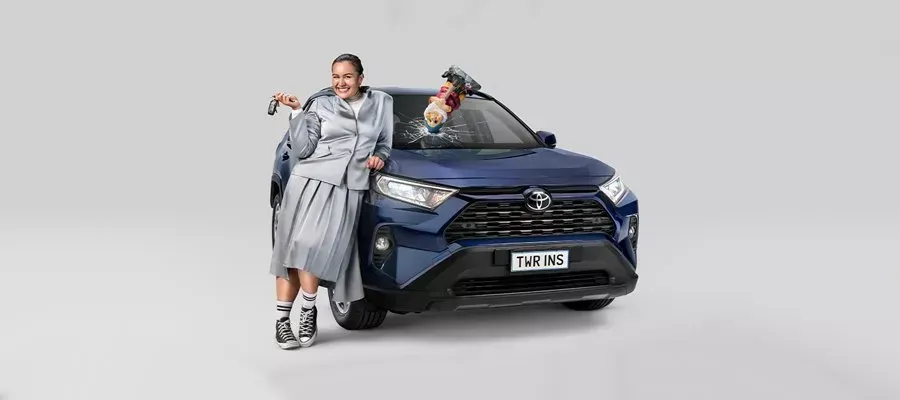 Woman leaning against blue car holding up keys gnome going through the windscreen