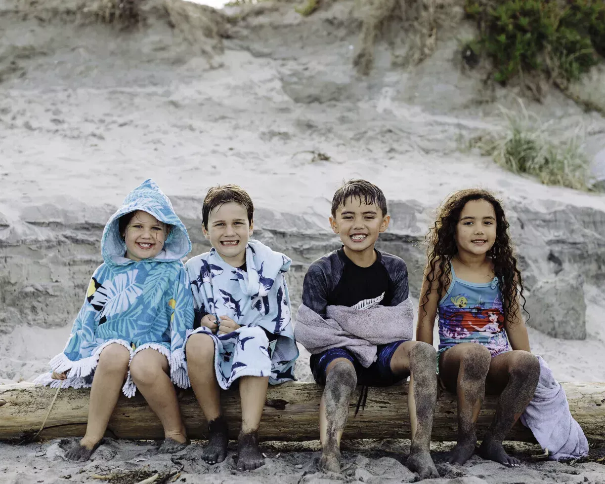 four kids sitting on a log at the beach