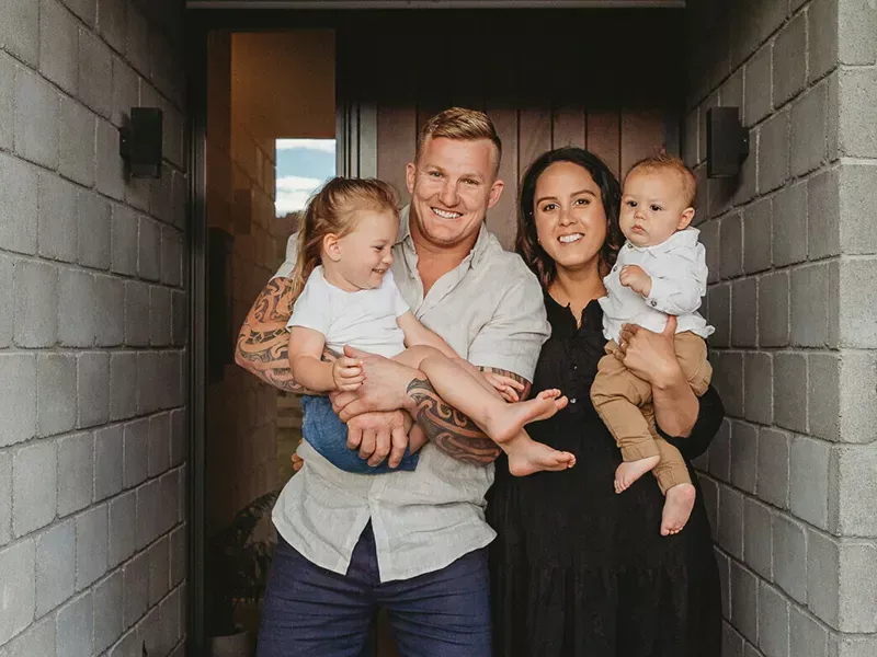 young family of four standing in front of door smiling