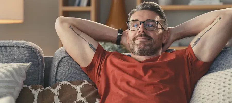 Man relaxing on the couch with hands up behind his head, thinking about Chubb lifetime reward discount.