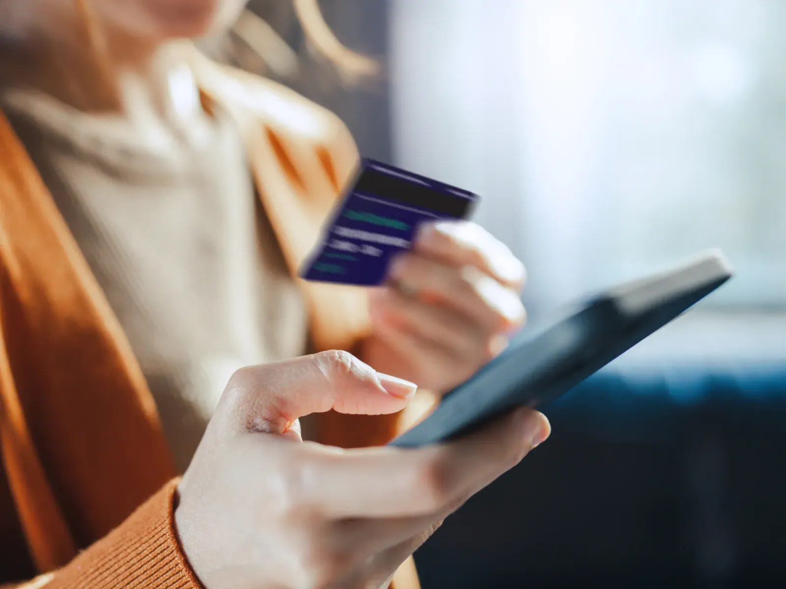 Person holding a card and smartphone, representing online payment security and scam awareness